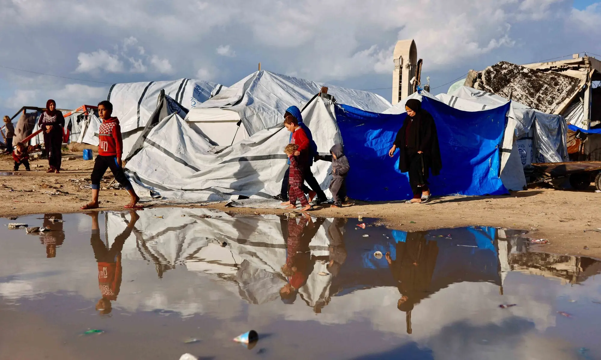 Displaced Palestinians walk past a large pool of rainwater accumulated near tent shelters, as the region faces rain and cold winter.&mdash;AFP