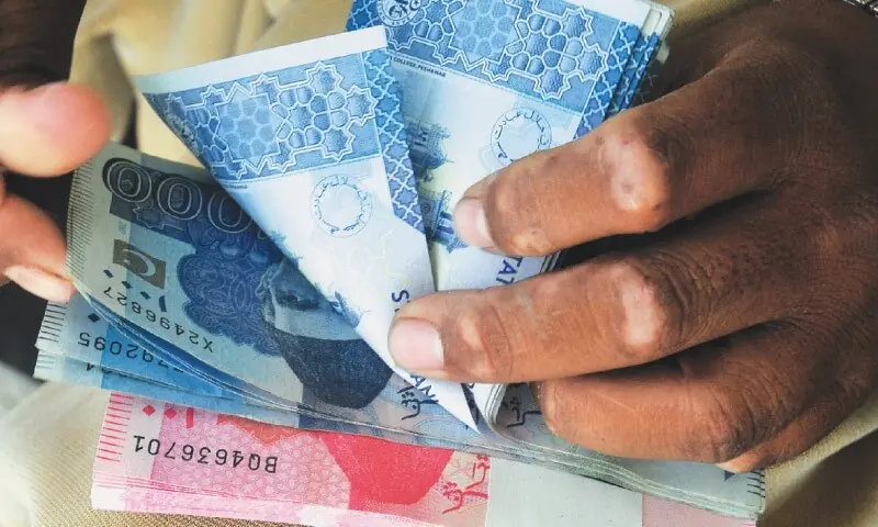 A man holds a bunch of Pakistani currency notes in this file photo. &mdash; White Star/File