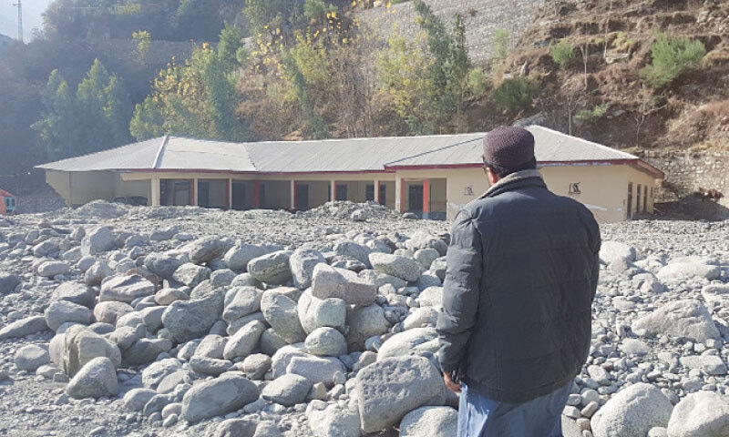 A man looks at a government high school partially buried under rocks and stones after 2022 flash floods in Ranowalia, Lower Kohistan. &mdash; Dawn
