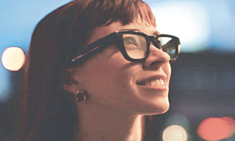 A person wearing glasses smiles while looking upward against a blurred backdrop of city lights. &mdash;Courtesy The Korea Herald