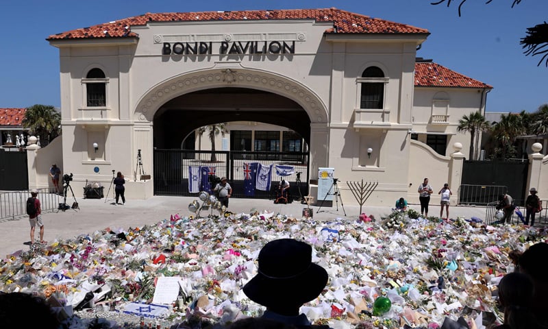 SYDNEY: Mourners stand near tributes piled together in front of the Bondi Pavilion, in memory of the victims of the deadly beach shooting.&mdash;AFP
