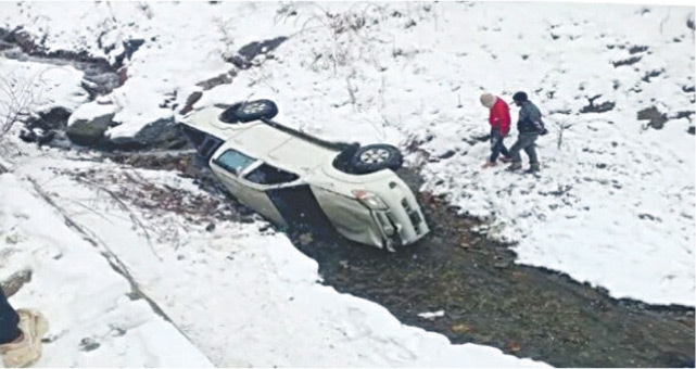  Two men stand near a vehicle which skidded off a snowy road in Oveerik village of Injigan valley, Chitral, on Tuesday. &mdash; Dawn 