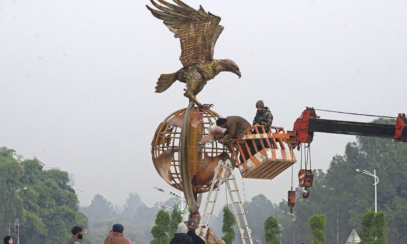 Workers install lights on a globe at Shaheen Chowk underpass before its inauguration in Islamabad on Wednesday. &mdash; Photo by Mohammad Asim
