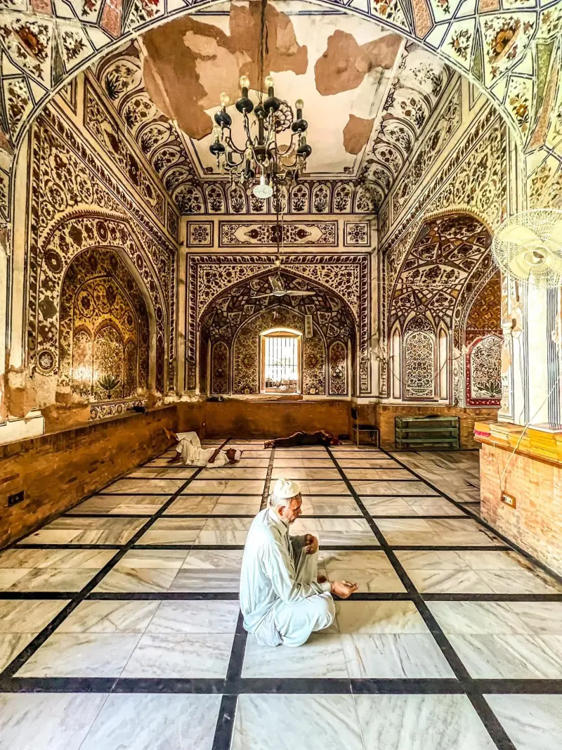 A worshipper sits inside the historic Mohabbat Khan Mosque. Amid fading frescoes and worn marble floors, the centuries-old mosque remains a place of solitude and devotion.