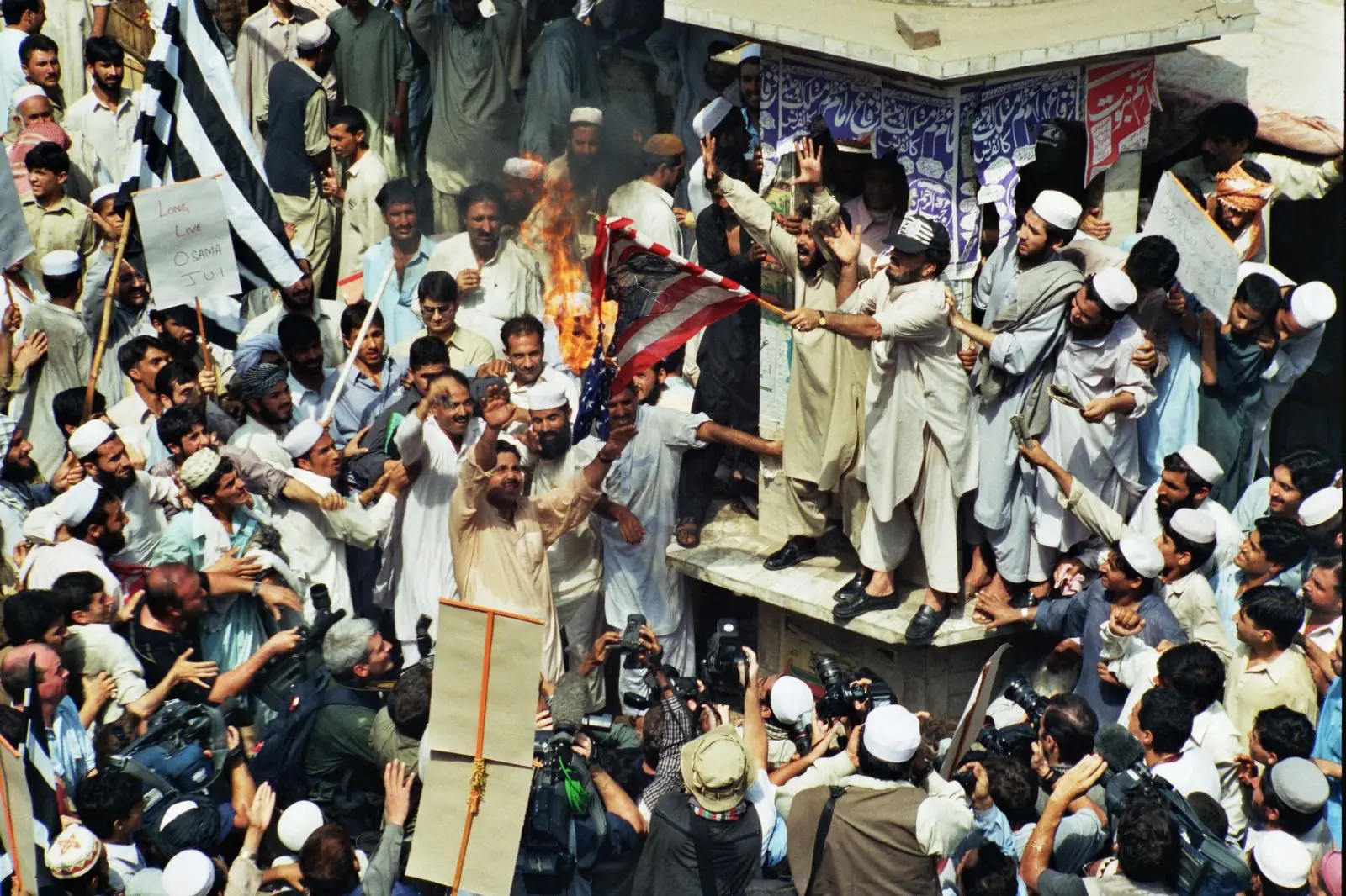 Supporters of a religious political party burn an American flag during a protest at Peshawar’s Martyrs’ Monument, erected in memory of members of the non-violent Khudai Khidmatgar movement killed by British forces. The moment underscores the contrast between a site rooted in peaceful resistance and later waves of political anger shaped by global events.