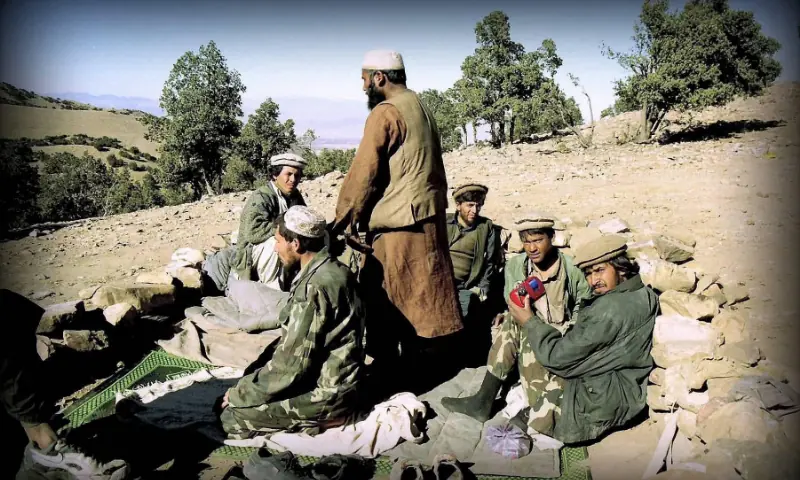 Tora Bora, Afghanistan: Foot soldiers rest during a pause in fighting. Some prepare for prayer, while one listens quietly to Indian songs on the All India Radio. Beyond labels such as Taliban or mujahid holy warrior, the image reveals the ordinary human contradictions of war — faith, fatigue, memory and music coexisting in a single moment.