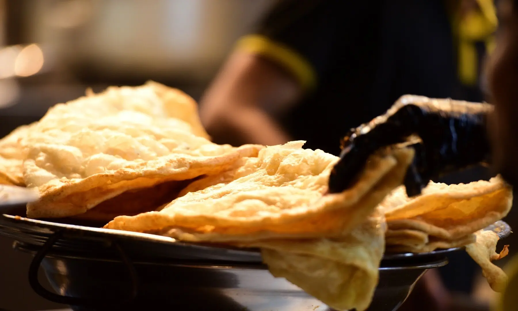 A vendor places piping hot pooris on a plate at Spicy Khan, Burns Road, a classic breakfast and snack favourite that draws Karachiites from dawn to late night. &mdash; Tahir Jamal/White Star