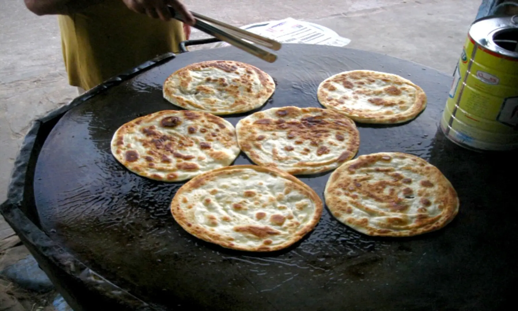 Golden parathas being fried on a large tawa at Burns Road, their flaky layers sizzling in ghee, a staple breakfast and late-night favourite for Karachiites. &mdash; Fahim Saddique/White Star