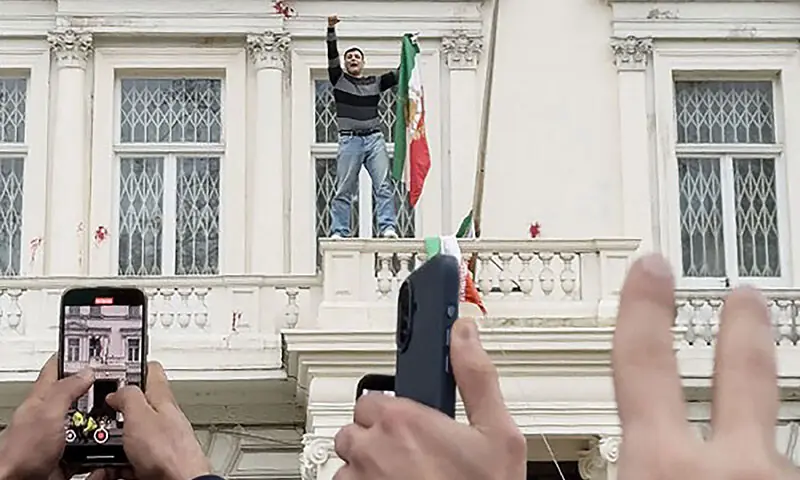 This screen grab taken from an anonymous user generated video via AFPTV on January 10 shows a protester holding Iran’s pre-1979 flag after pulling down the country’s current flag, on the balcony of Iran’s embassy in central London. —  AFP