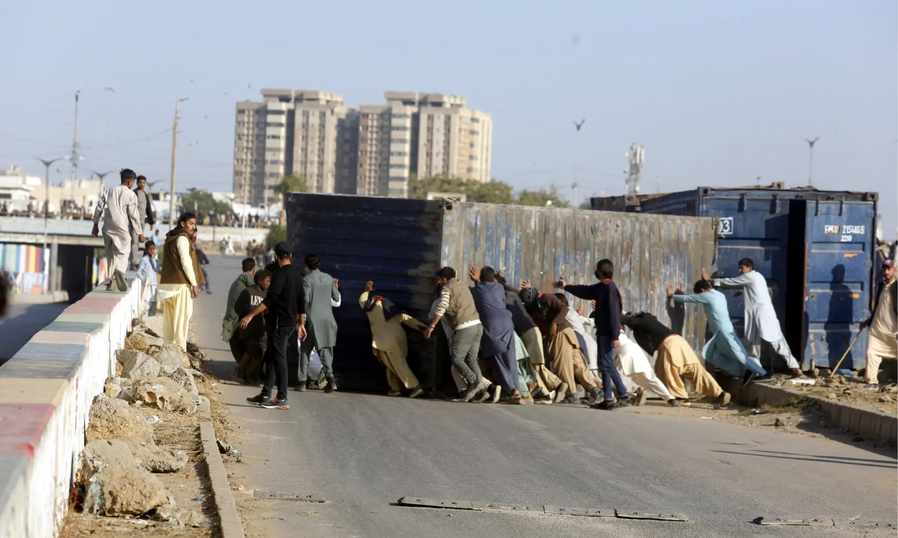 People push aside containers that had been placed to block a route in Karachi. — Shakil Adil/ White Star