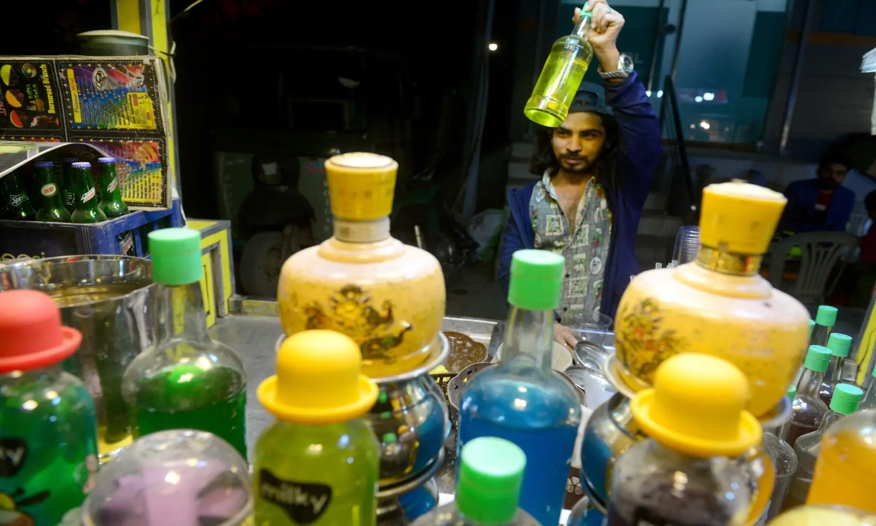 A vendor prepares colourful drinks at his stall in Hussainabad, adding a vibrant touch to the lively street food scene. &mdash; Tahir Jamal