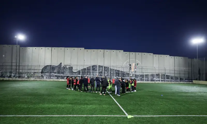 [3/5] Palestinian camp football team stands in a field ahead of game, next to West Bank barrier separating Aida refugee camp from Jerusalem, in the Israeli-occupied city of Bethlehem on January 11, 2026. &mdash; Reuters