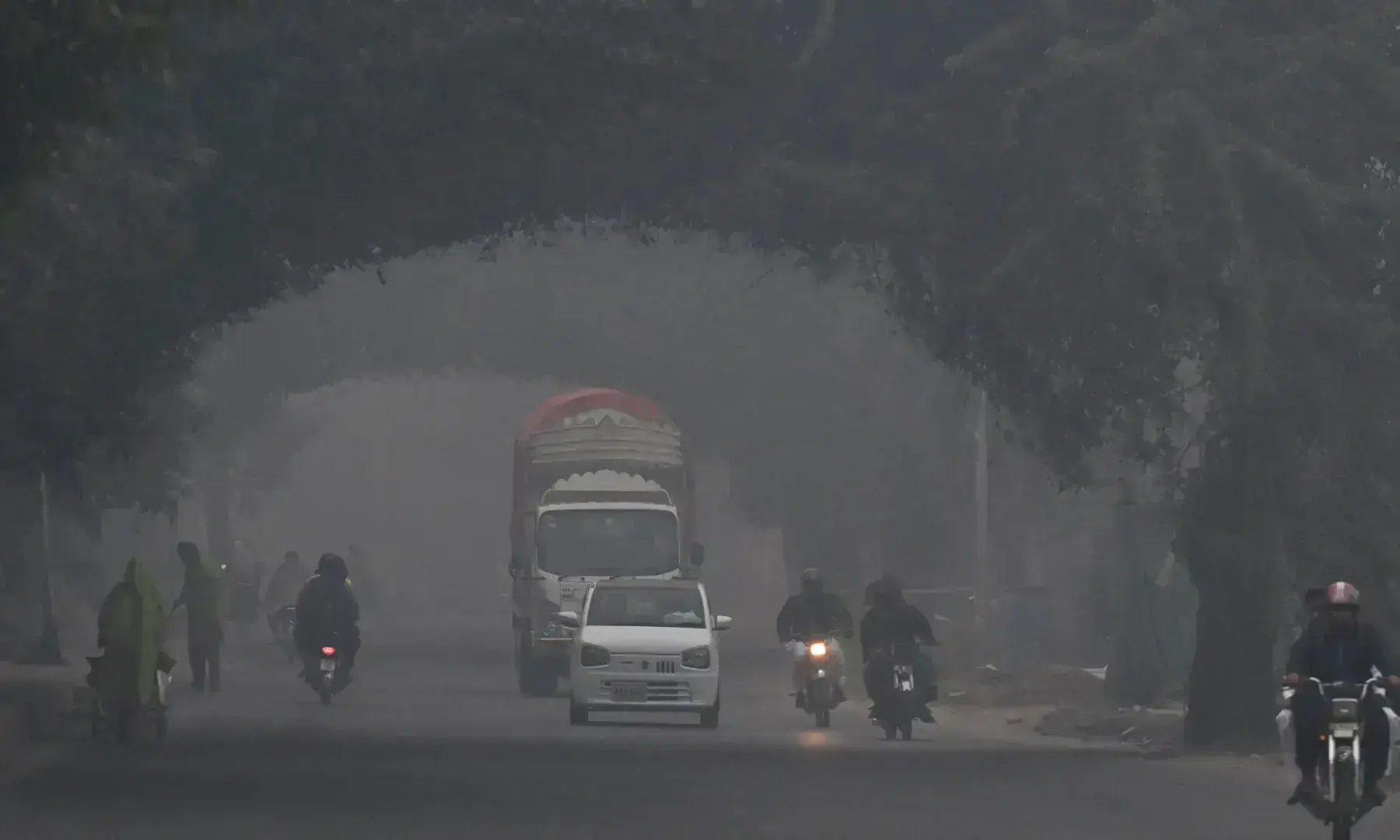 Commuters ride along a street amid dense smog in Lahore on Nov 1, 2025. &mdash; AFP/File
