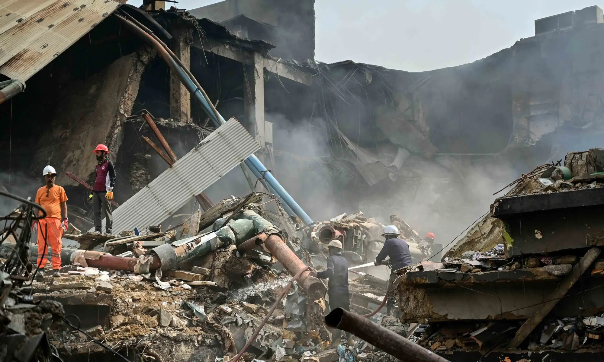 Fire fighters and rescue workers perform a cooling operation amid the debris after a massive fire at a shopping mall in Karachi on January 19. — AFP