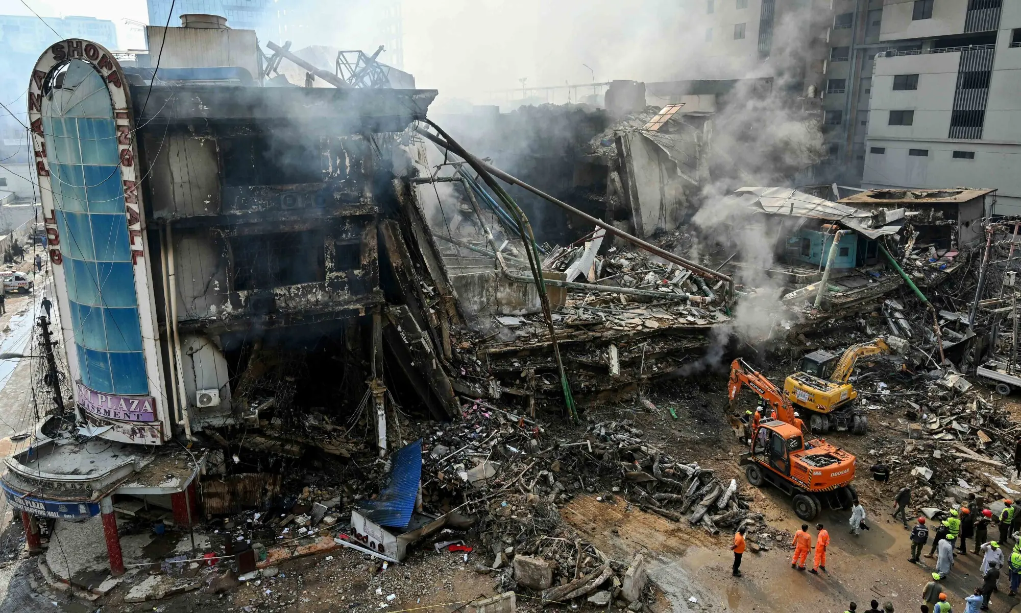 TOPSHOT - Rescue workers search amid the debris using excavators after a massive fire at a shopping mall in Karachi on January 19, 2026. (Photo by Asif HASSAN / AFP)