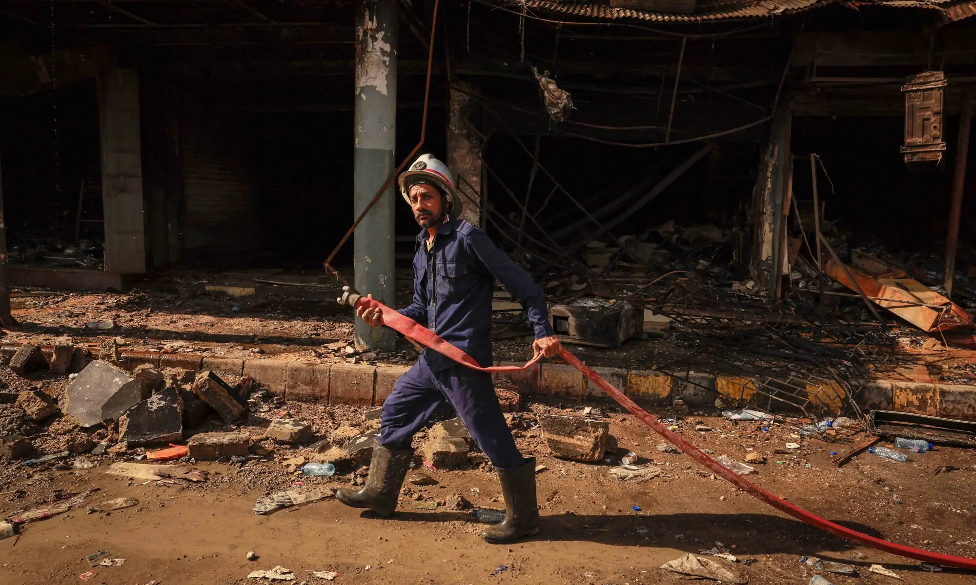 A firefighter pulls a water pipe at the site, following a massive fire that broke out in the Gul Plaza Shopping Mall in Karachi on January 20. &mdash; Reuters