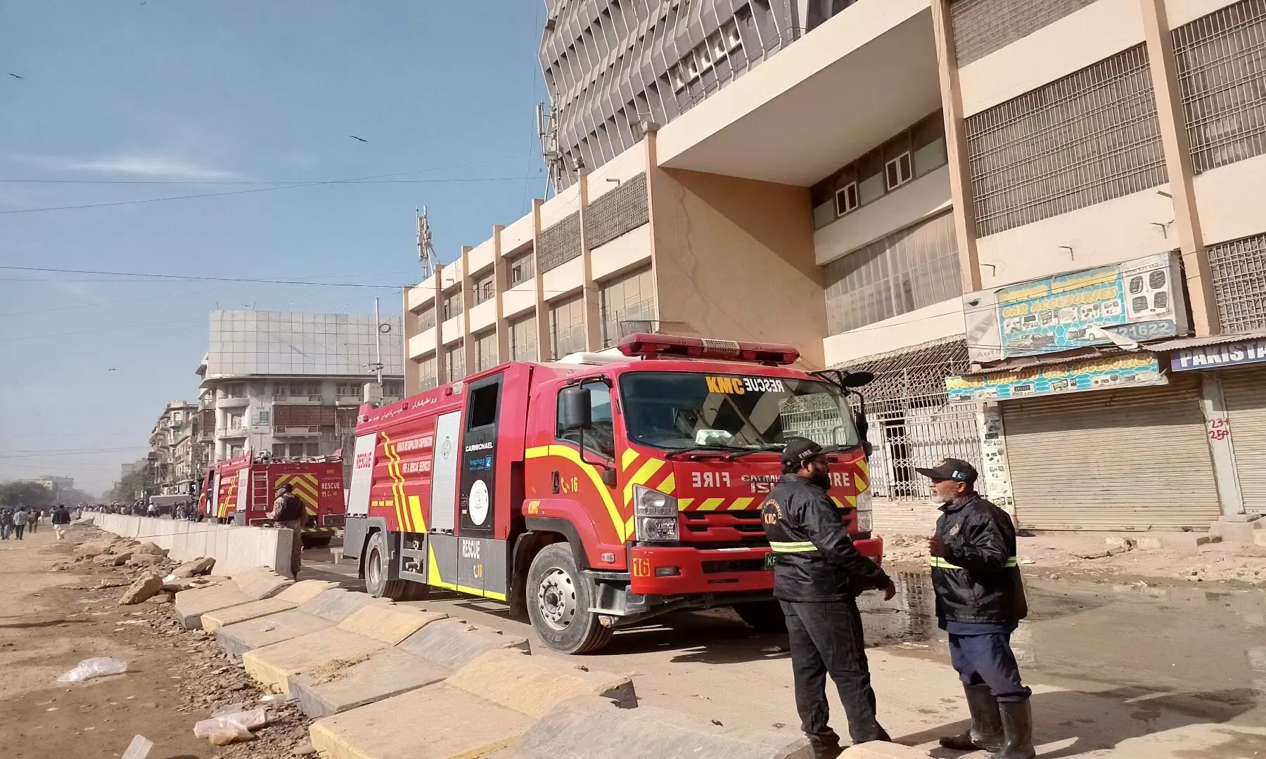 Members of the fire crew stand next to two fire trucks parked near Gul Plaza on MA Jinnah Road in Karachi. &mdash; Shazia Hasan