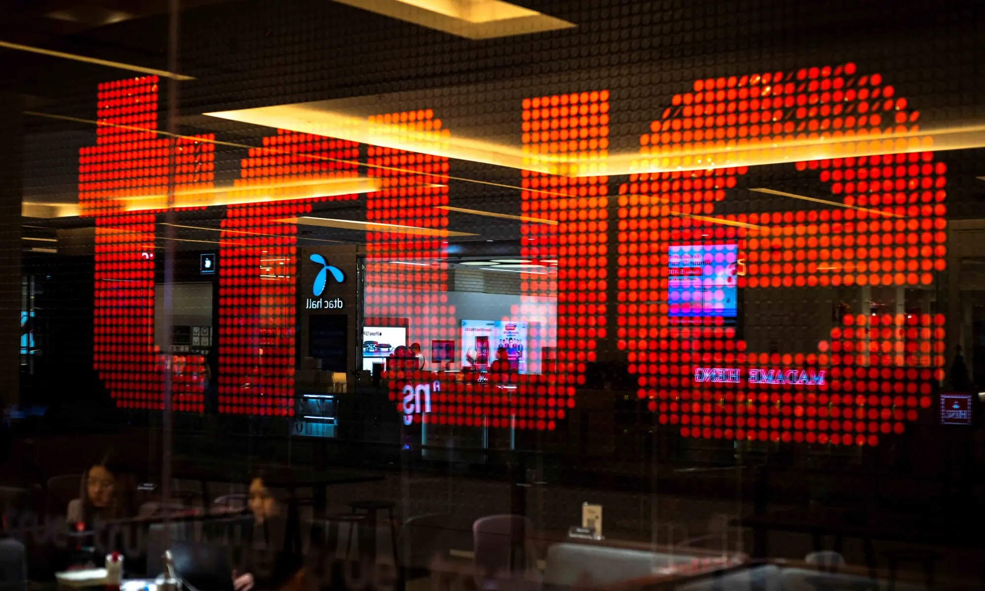 People are silhouetted in front of an electronic screen showing logo of the True Corp. at a department store in Bangkok, Thailand, November 22, 2021. &mdash; Reuters