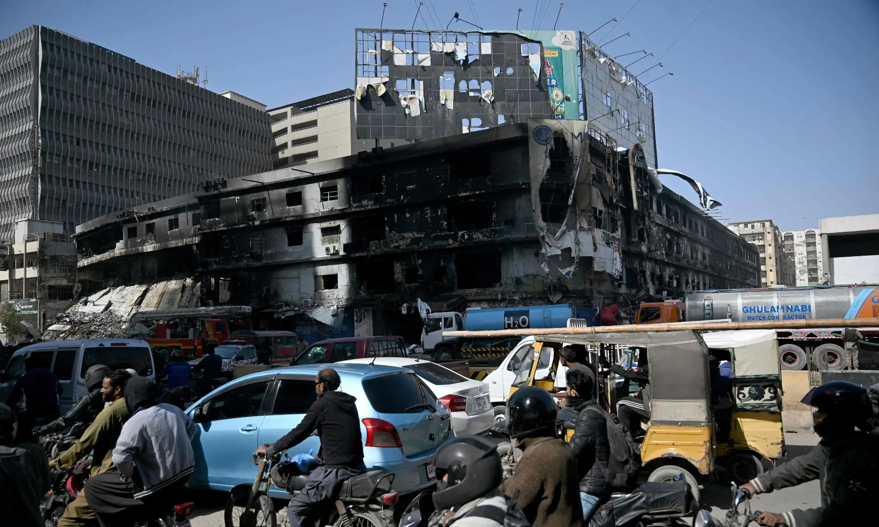 Commuters ride past the charred Gul Plaza shopping mall in Karachi on Jan 23, 2026. &mdash; AFP