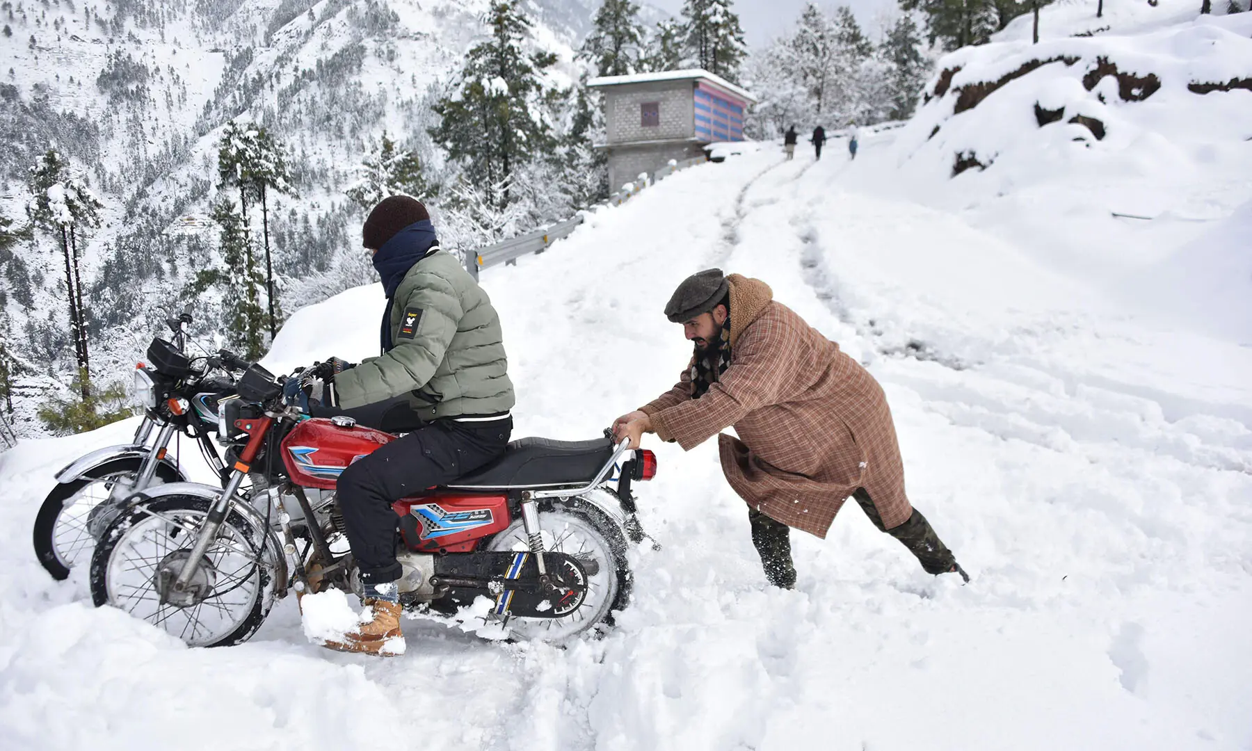 A man helps a motorcyclist to steer out of a snow-covered road on the outskirts of Muzaffarabad, Azad Jammu and Kashmir on January 23. &mdash; AFP