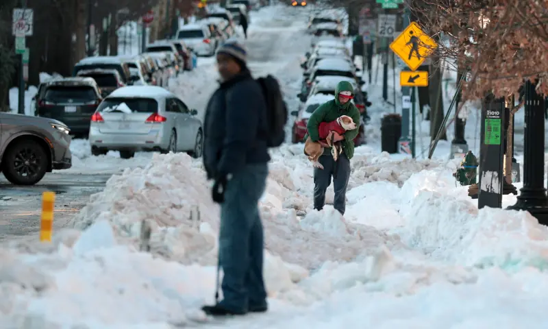A man carries his dog as they make their way through snow and ice, in the aftermath of a major winter storm, in Washington, DC, US on January 27, 2026. &mdash; Reuters