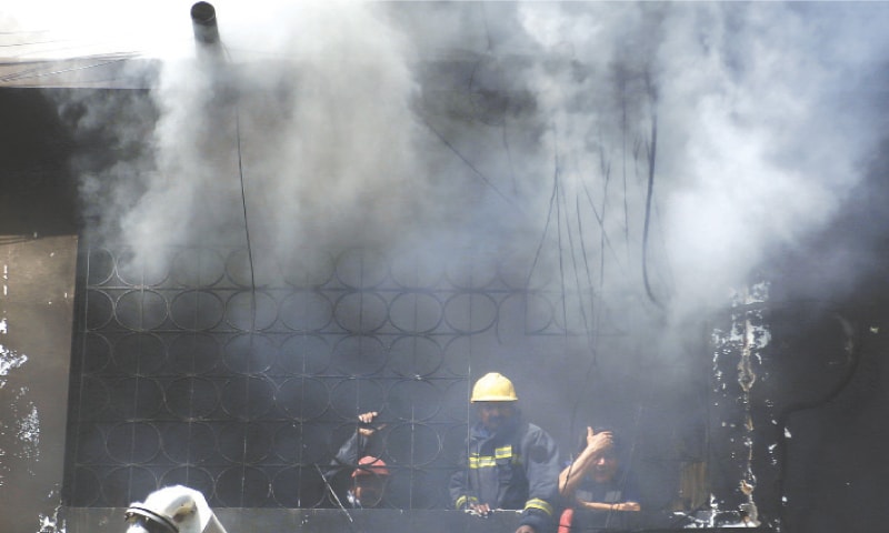 Rescue workers and firefighters working inside the still-smouldering Gul Plaza, pause to catch their breath on a window sill.&mdash;Shakil Adil / White Star