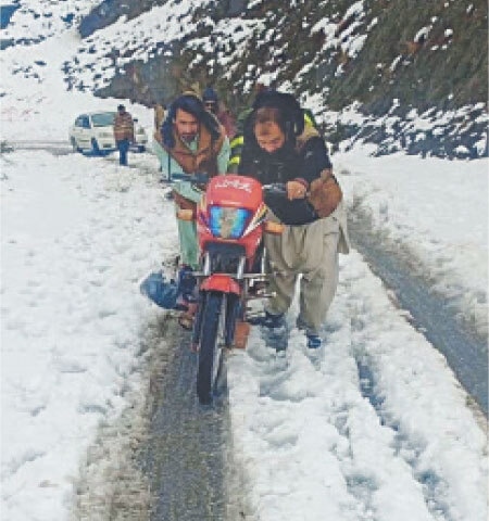 A man assists a motorcyclist on a snow-covered road in the mountainous Kohi Sar locality of Barang tehsil in Bajaur district on Friday. &mdash; Photo by Anwarullah Khan