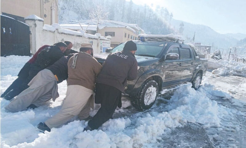 Policemen push a vehicle on snow-covered road near University of Shangla on Saturday. &mdash; Dawn