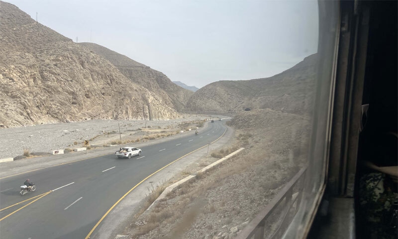 A man sitting in the cargo bed of a vehicle waves at the Jaffar Express as it makes its journey through the Kolpur area of Balochistan in December 2025