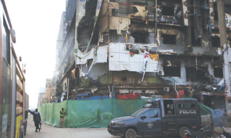 A police vehicle is parked in front of Gul Plaza as an official secures the outer parameter of the gutted structure with yellow tape. 
&mdash;Shakil Adil / White Star