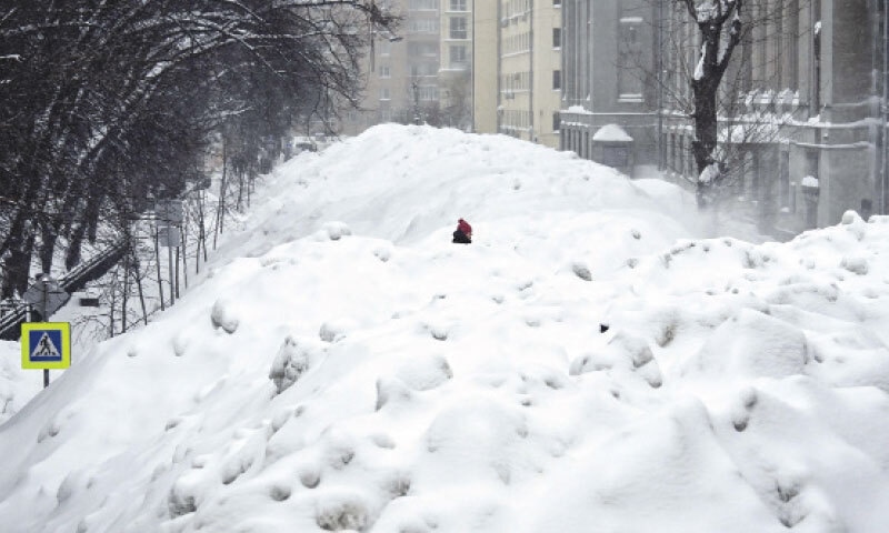 A pedestrian crosses a street used for temporary snow storage in Moscow.&mdash;AFP
