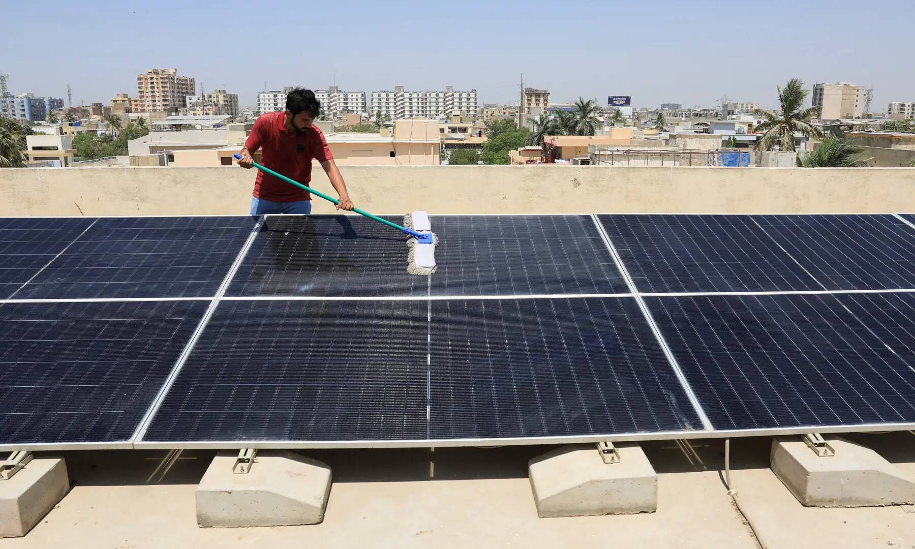 A man uses a wiper to clean the solar panels installed on the rooftop of his home in Karachi on April 5, 2025. &mdash; Reuters/File
