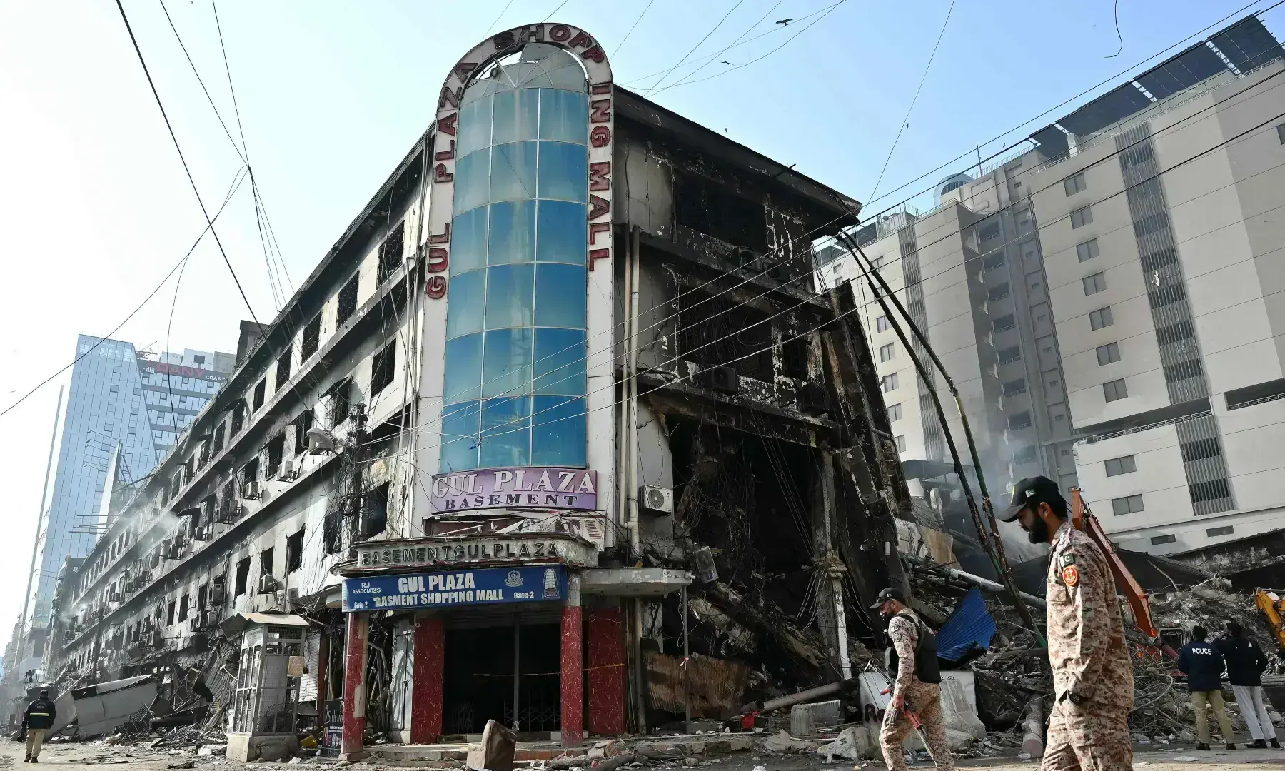 Paramilitary personnel walk past charred remains of the Gul Plaza shopping mall in Karachi on Jan 22, 2026. &mdash; AFP/File