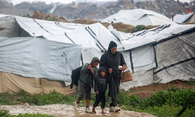 A woman and two boys walk along a muddy road past tents housing people displaced by war, after heavy rain at the Bureij camp for Palestinian refugees in the central Gaza Strip on February 24, 2026. — AFP A woman and two boys walk along a muddy road past tents housing people displaced by war, after heavy rain at the Bureij camp for Palestinian refugees in the central Gaza Strip on February 24, 2026. — AFP