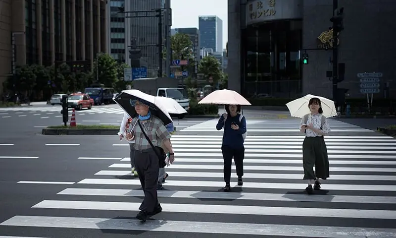 People hold umbrellas as they walk along a street in Tokyo. &mdash; AFP/File