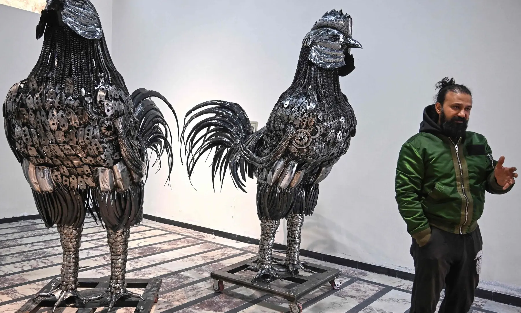 This photograph taken on December 29, 2025 shows sculptor Ehtisham Jadoon standing next to rooster sculptures made from scrap metal at his studio on the outskirts of Islamabad. &mdash; AFP