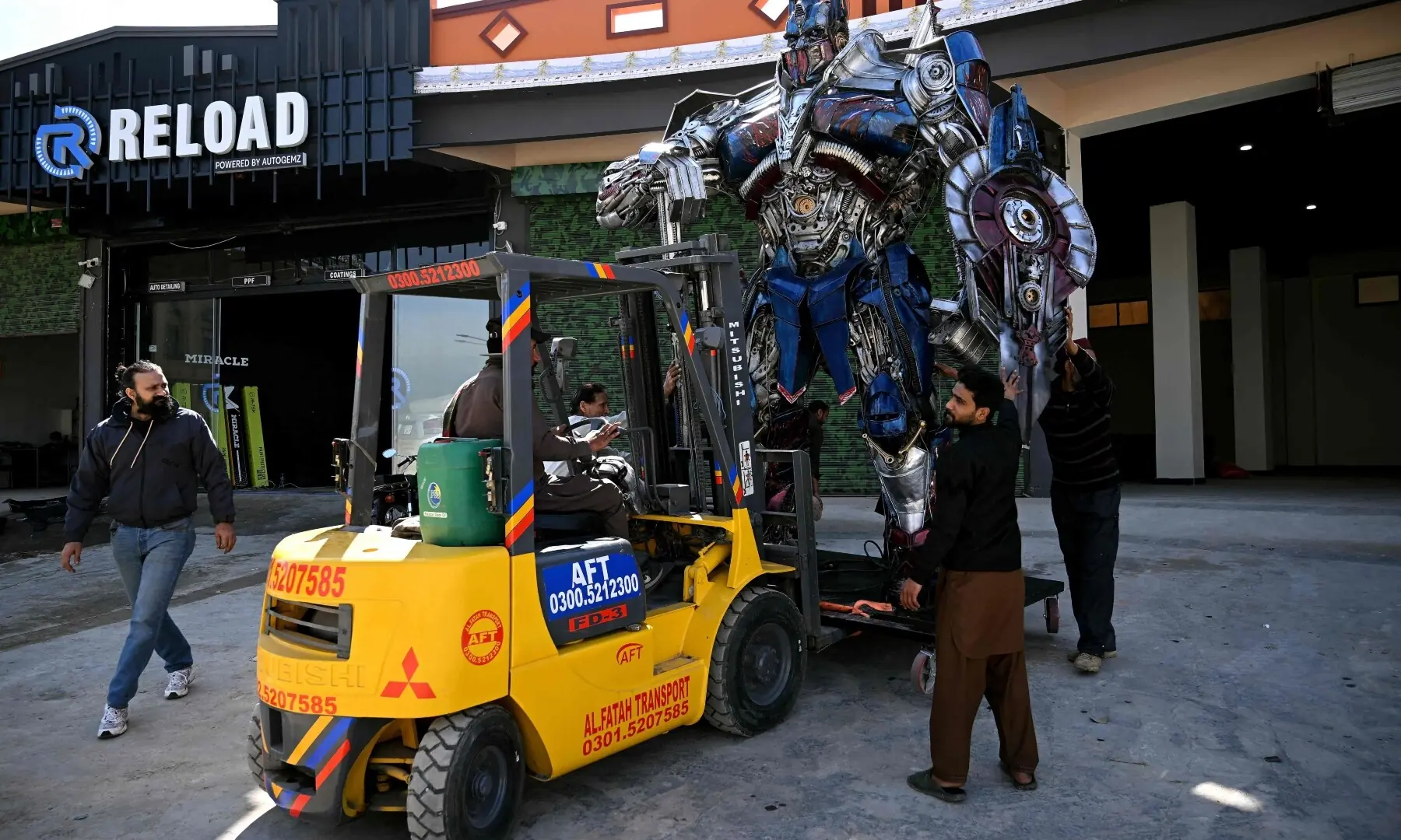 This photograph taken on February 12, 2026 shows workers carrying a model of Optimus Prime, a film character from Transformers, made from scrap metal by sculptor Ehtisham Jadoon (L) at his studio on the outskirts of Islamabad. &mdash; AFP