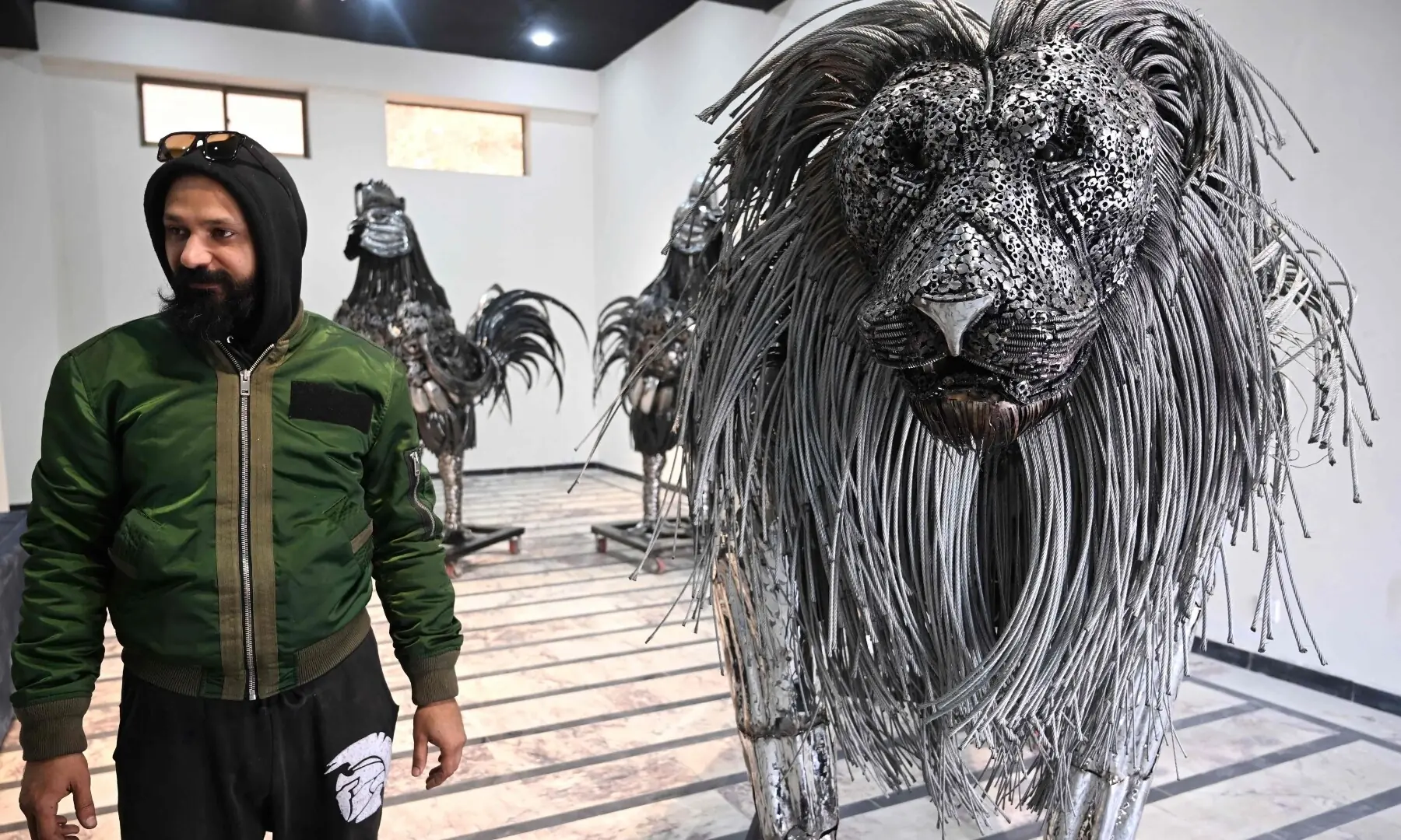 This photograph taken on December 29, 2025 shows sculptor Ehtisham Jadoon posing with his creation made from scrap metal, a lion with a mane of twisted steel, at his studio on the outskirts of Islamabad. &mdash; AFP