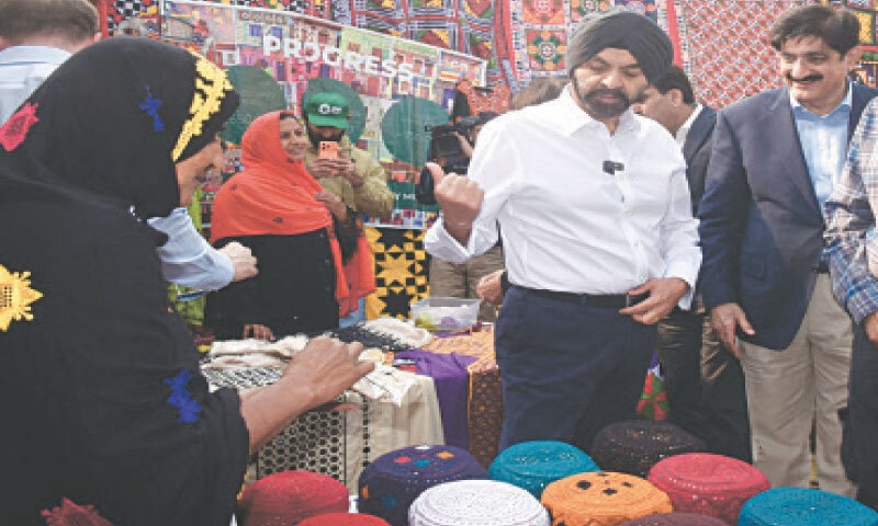 World Bank President Ajay Banga, along with Sindh Chief Minister Murad Ali Shah, interacts with a woman showing him traditional Sindhi handicrafts at a community centre in Bahwal Jat village.&mdash;Dawn