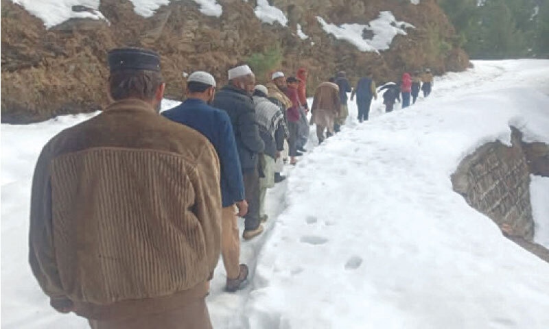 Residents take a walk on a road blocked due to recent snowfall in Torghar. &mdash; Dawn