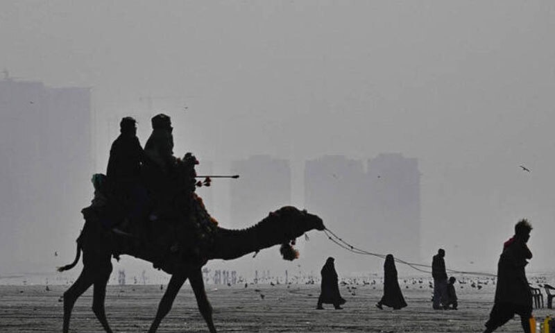 This photograph, taken on January 10, 2026, shows people riding a camel amid dense smog at the Seaview Beach in Karachi, as pollution levels in Pakistan continue to hit record highs | AFP