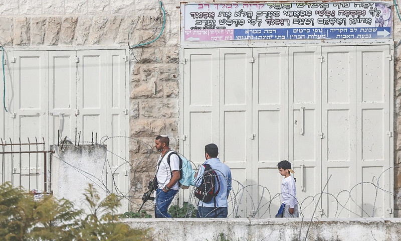 HEBRON: Armed Israeli settlers walk near the settlement of Abraham Avino in this Israeli-occupied West Bank city.—AFP HEBRON: Armed Israeli settlers walk near the settlement of Abraham Avino in this Israeli-occupied West Bank city.—AFP