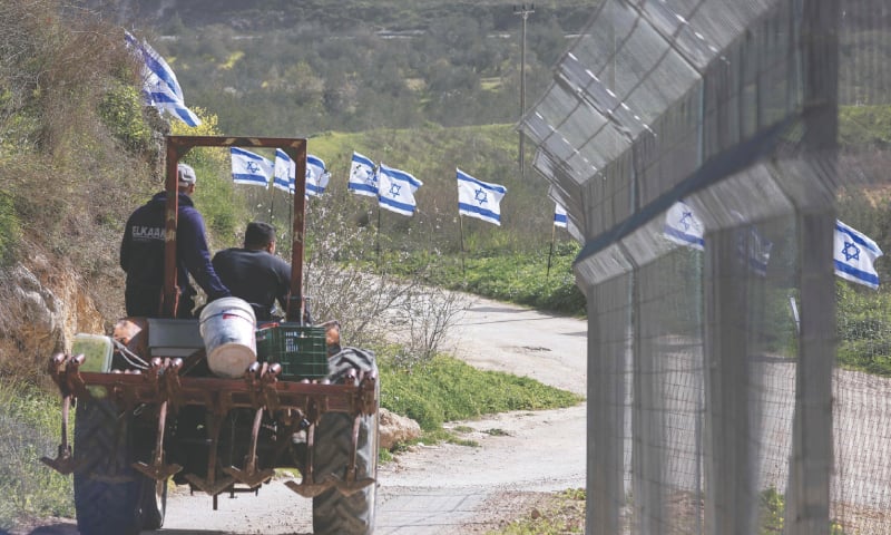 NABLUS: Palestinian farmers from Burqa village drive their tractor past a fence with Israeli flags installed by Jewish settlers, after Israel announced its control over several parts of the occupied West Bank.&mdash;AFP
