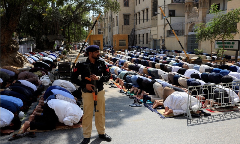 A policeman stands alert as people offer Friday prayers on the road in front of a mosque.—Reuters A policeman stands alert as people offer Friday prayers on the road in front of a mosque.—Reuters