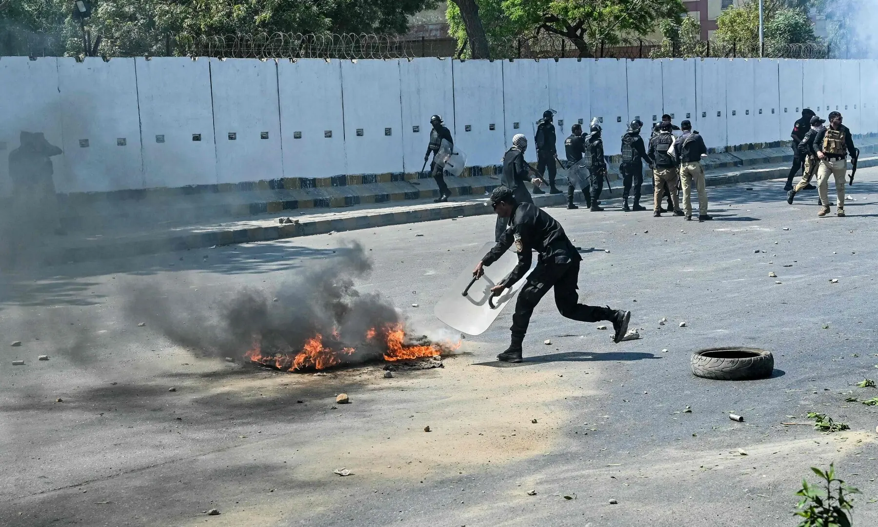 A police personnel douses fire during a clash with protesters as they attempt to storm the US consulate in Karachi on March 1, 2026. &mdash; AFP