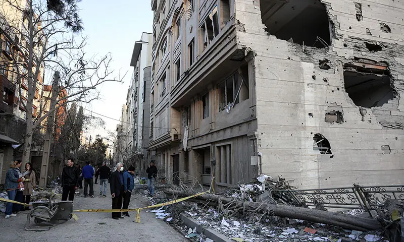 Residents stand in a street beside damaged residential buildings near Niloufar Square in Tehran, Iran on March 2. &mdash; AFP