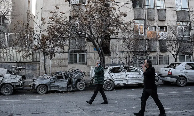 Two men walk past destroyed cars near Niloufar Square in Tehran, Iran on March 2. &mdash; AFP