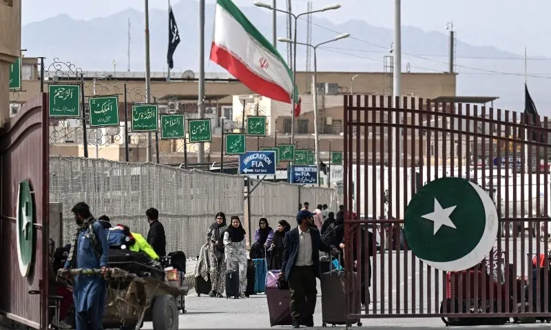 Pakistani nationals walk across the Pakistan-Iran border after returning from Iran as an Iranian national flag (C) flies at half-mast at Taftan, Balochistan province on March 2, 2026 after the death of Iran&rsquo;s supreme leader Ayatollah Ali Khamenei amid US-Israel strikes. &mdash;AFP/File