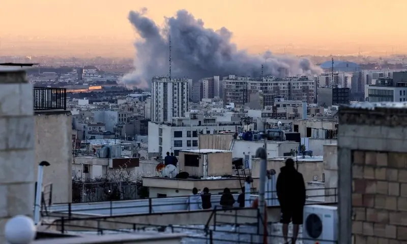 A person stands on a rooftop watching a plume of smoke rise after a strike on Tehran, Iran on March 3. &mdash; AFP