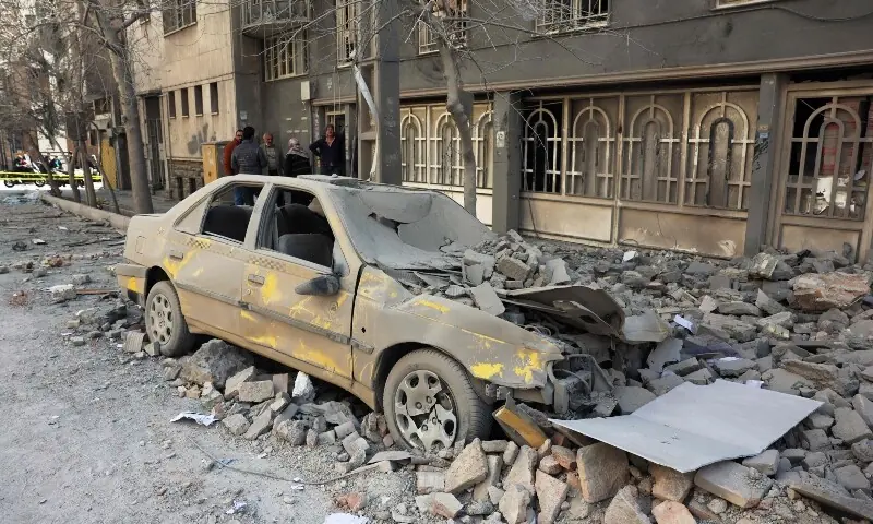 Residents stand near the debris of a building and a damaged car following airstrikes in central Tehran, Iran on March 4. &mdash; AFP